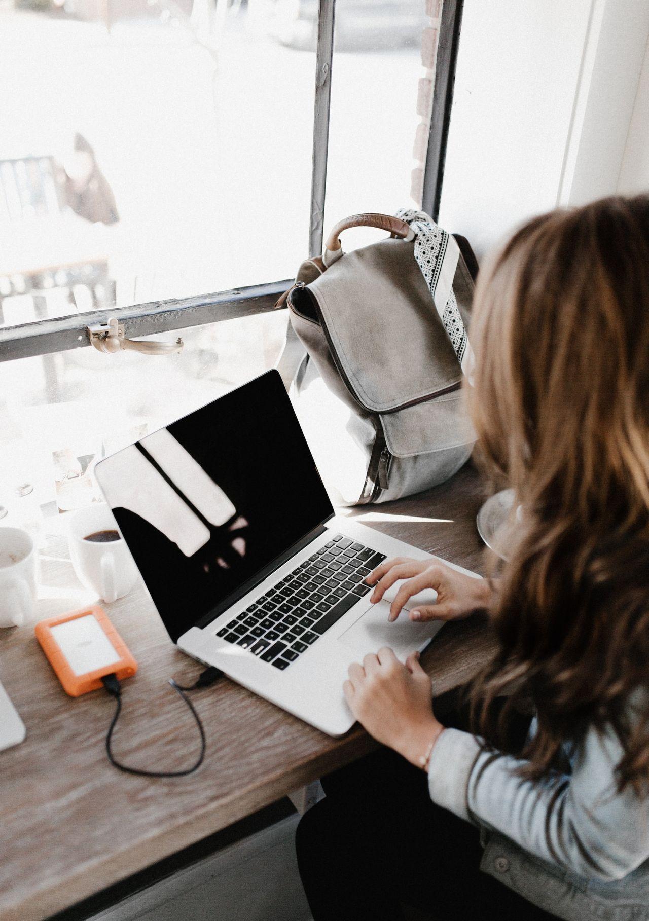 girl wearing grey long-sleeved shirt using MacBook Pro on brown wooden table